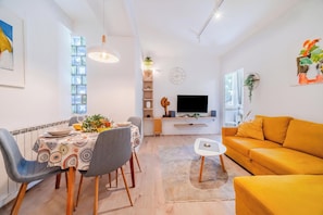 Uma sala moderna com área de jantar, sofá, televisão e uma planta.