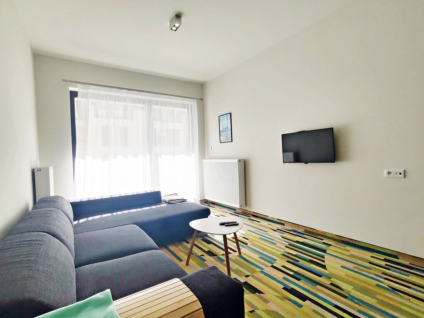 A modern living room with a sofa, a small round table, a TV mounted on the wall, and a patterned floor.