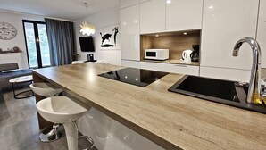 A modern kitchen with a wooden countertop, two white bar stools, a built-in microwave, and a coffee maker. - Baltic Park Molo by Baltic Home (Swinoujscie)