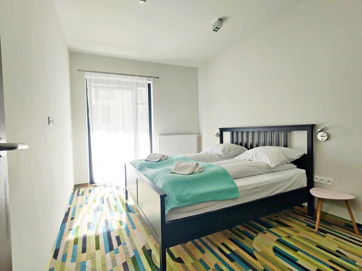 Une chambre à coucher avec un lit, un radiateur, une fenêtre avec des rideaux et un sol à motifs.