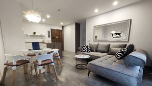 A modern living room with a grey sectional sofa, a round dining table with white chairs, a small side table, and a large mirror on the wall. - Baltic Park Molo by Baltic Home (Swinoujscie)