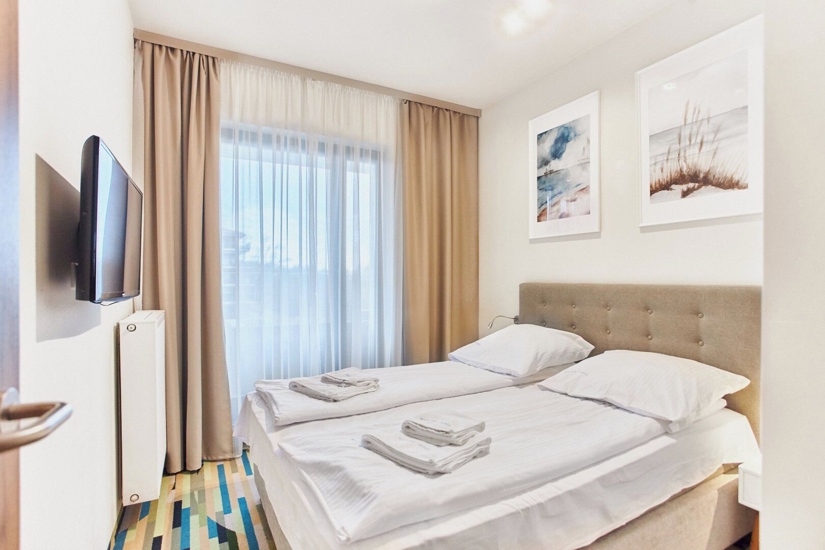 A hotel room with a bed, a TV, and two paintings on the wall.