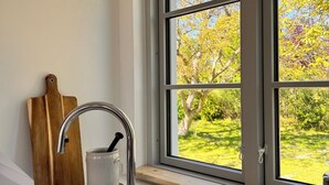 A kitchen with a window, a wooden cutting board, a white mug, and a stainless steel faucet. - Sommerby Sky - near the beach, shower, desk, top floor, EV charging station (Brodersby)