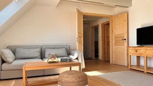 A modern living room with a sofa, a coffee table, a television, and wooden doors. - Sommerby Sky - near the beach, shower, desk, top floor, EV charging station (Brodersby)