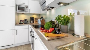 Een moderne keuken met witte kasten, een ingebouwde magnetron, een koffiezetapparaat en een snijplank met verse groenten.
