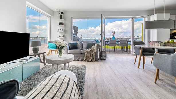 Een ruime woonkamer met een groot raam, een bank, een eettafel en een televisie.