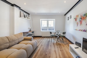 Una sala de estar moderna con un sofá, una mesa de comedor con sillas, un televisor y una ventana.