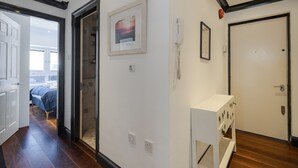 A hallway with a bed in the background, a framed picture, a phone, and a door. - Covent Garden’s Secret, by Veeve (London)