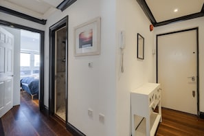 Um corredor com uma cama ao fundo, um quadro, um telefone e uma porta.