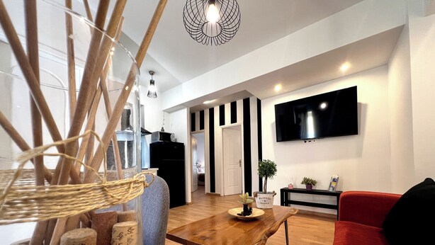 A modern living room with a wooden dining table, a red sofa, and a TV mounted on the wall.