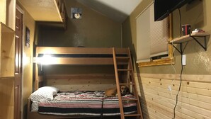 Een stapelbed met een ladder, een aan de muur bevestigde televisie en een raam met jaloezieën.