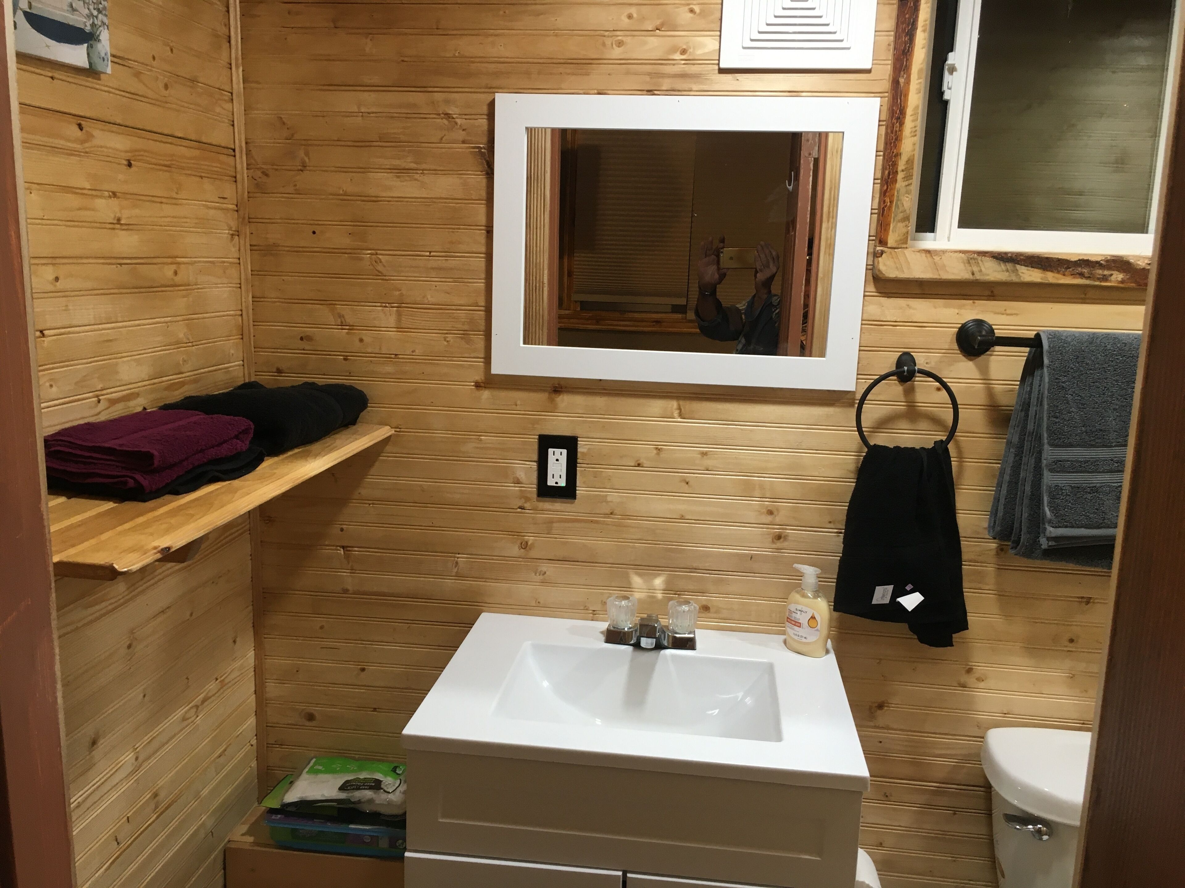 Une petite salle de bain aux murs lambrissés, avec un lavabo blanc, un miroir, un porte-serviettes et des toilettes.