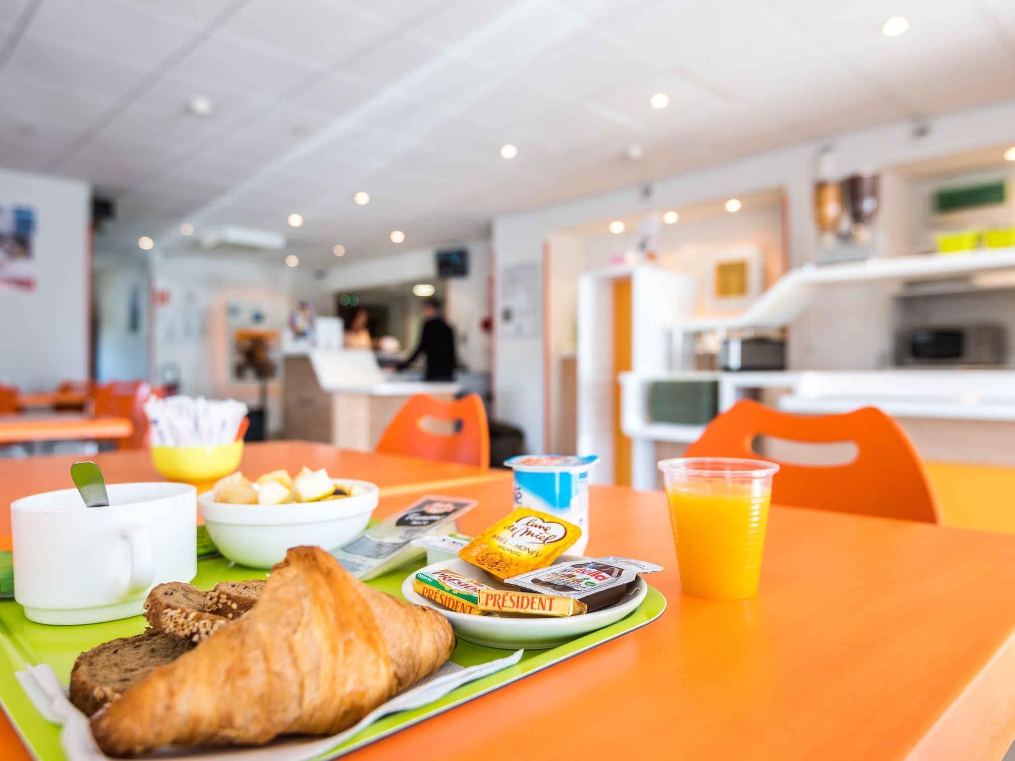 A breakfast setting with a croissant, yogurt, juice, and a sandwich on a table.