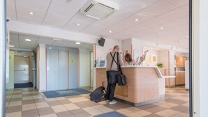 Ein Hotel-Empfangsbereich mit Check-in-Schalter, Wartebereich und einem sichtbaren Aufzug.