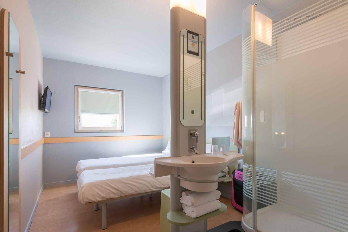 Une chambre d’hôtel comprenant un lit, un lavabo, un miroir, une fenêtre et un espace douche.