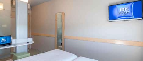 A hotel room with a bed, a TV mounted on the wall, a mirror, and a laptop on a stand.