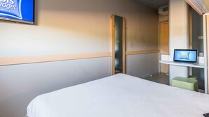 Ein Hotelzimmer mit Bett, Wandfernseher, Laptop auf einem kleinen Tisch und Spiegel.