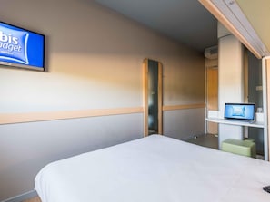 A hotel room with a bed, a television mounted on the wall, a laptop on a small table, and a mirror. - Ibis Budget Ambérieu-En-Bugey Château-Gaillard (Chateau-Gaillard)