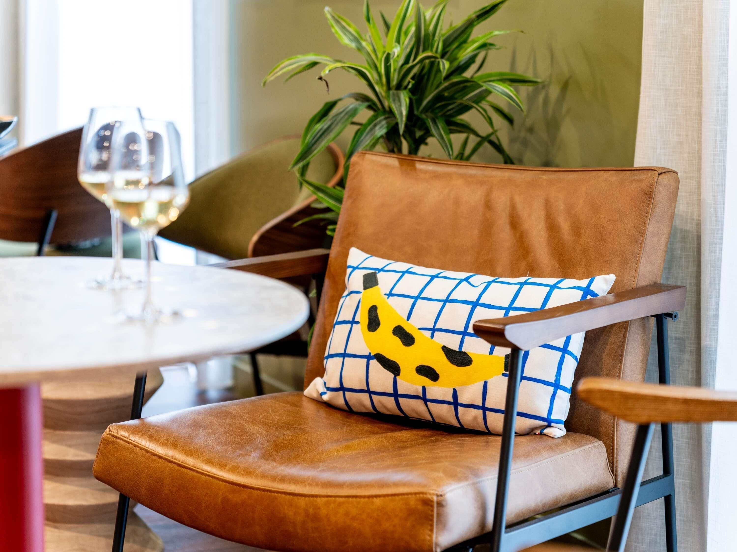 Un fauteuil en cuir marron avec un coussin bleu et blanc orné d’un motif représentant une banane jaune.