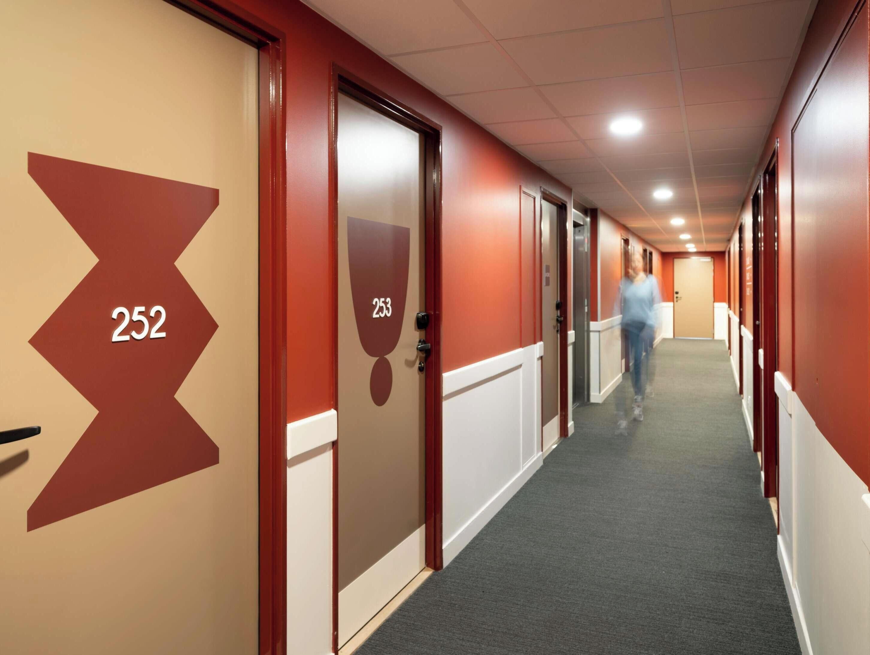 A corridor with doors numbered 252 and 253, carpeted flooring, and a person walking.