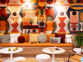 Uma sala de estar moderna com uma obra de arte abstrata colorida na parede, um sofá com almofadas de vários desenhos e uma mesa de centro com uma revista e um copo.