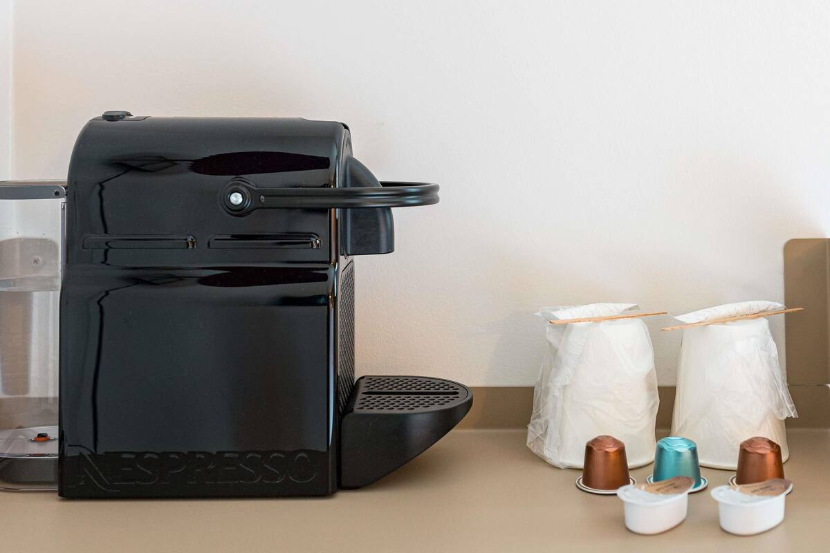 Una máquina de café Nespresso negra con una bandeja de goteo, una cafetera y varias cápsulas de café sobre una encimera.