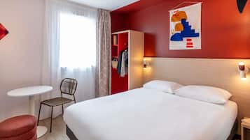 Habitación de hotel con cama, una mesita, una silla, armario y ventana con cortinas.