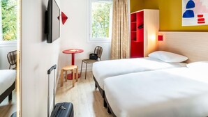 Habitación de hotel con dos camas, televisión, una mesita con una silla, un armario rojo y una ventana con cortinas.