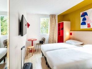 A hotel room with two beds, a TV, a small table with a chair, a red cabinet, and a window with curtains. - ibis Styles Prevessin Geneve Airport (Prevessin-Moens)