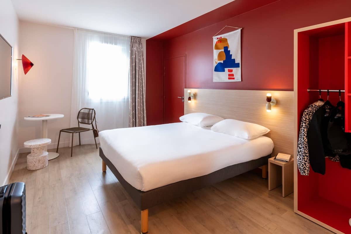Una habitación de hotel moderna con una cama, un escritorio pequeño, una silla y un armario.