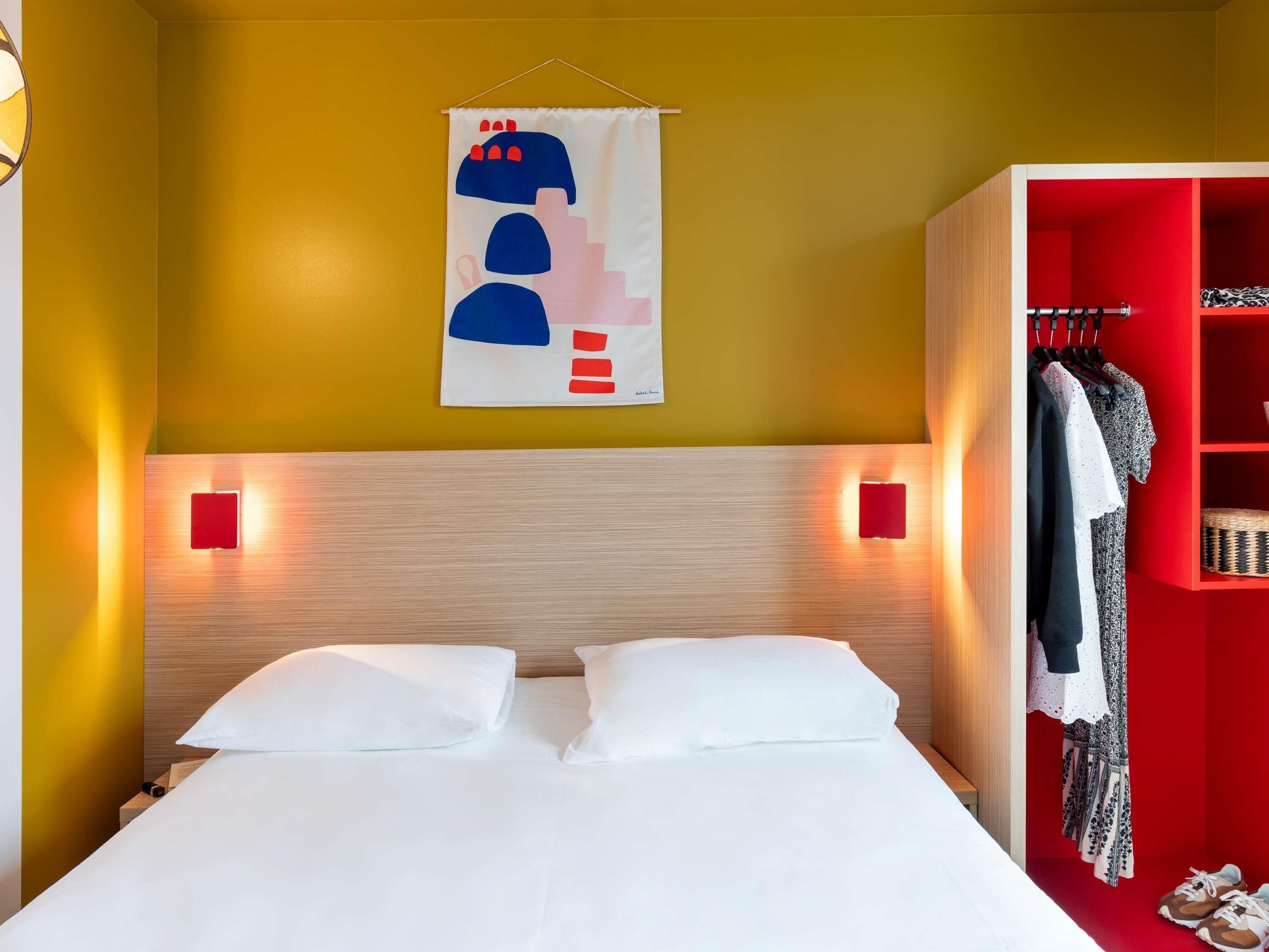 A hotel room with a bed, a wardrobe, and a wall-mounted artwork.