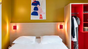 A hotel room with a bed, a wardrobe, and a wall-mounted artwork.
