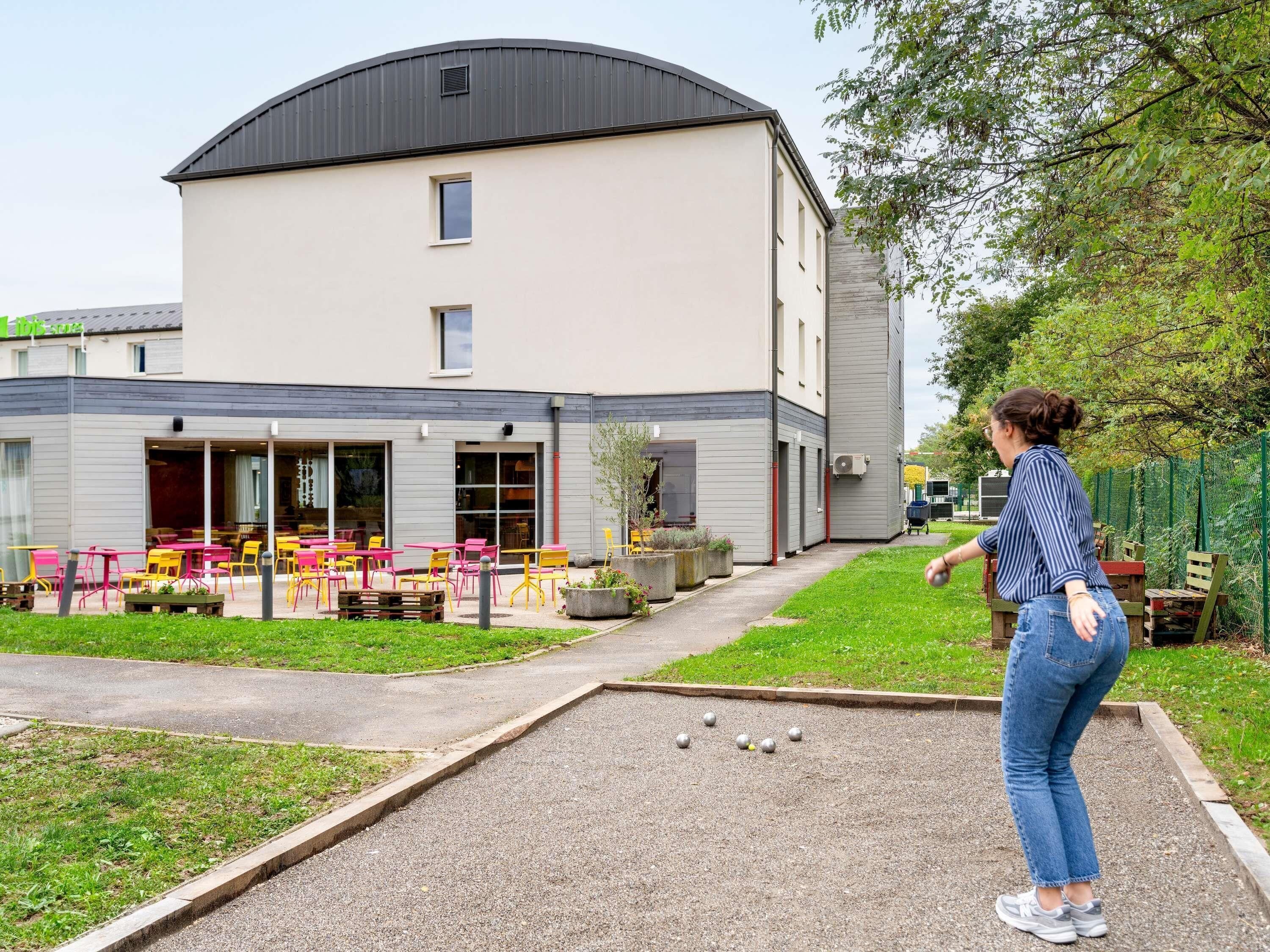 Un edificio con techo plano, un espacio al aire libre techado con mesas y sillas, y un sendero pavimentado.