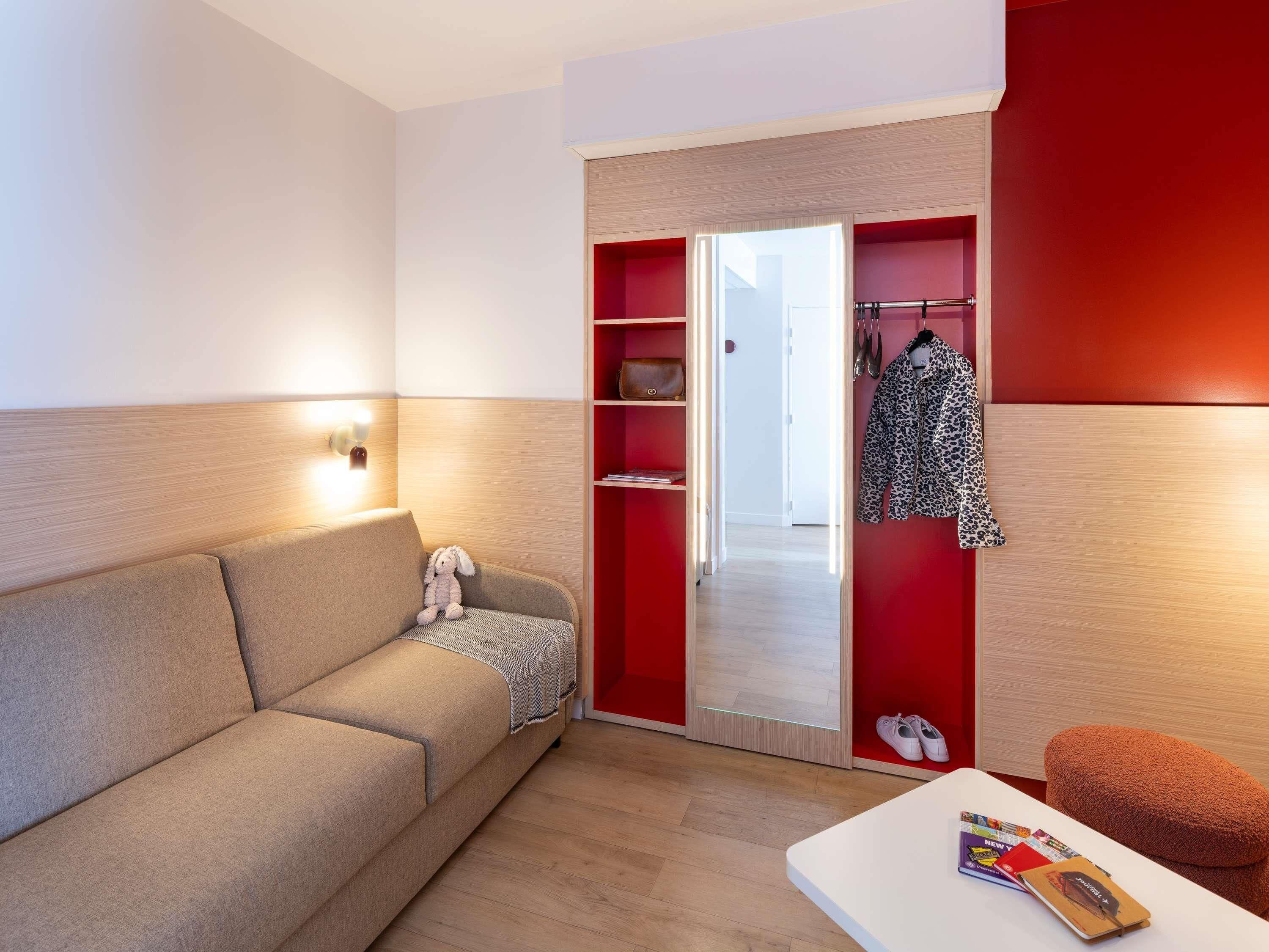 Ein modernes Zimmer mit einer Couch, einem kleinen Tisch mit Zeitschriften, einem roten Kleiderschrank und einer weißen Wand.