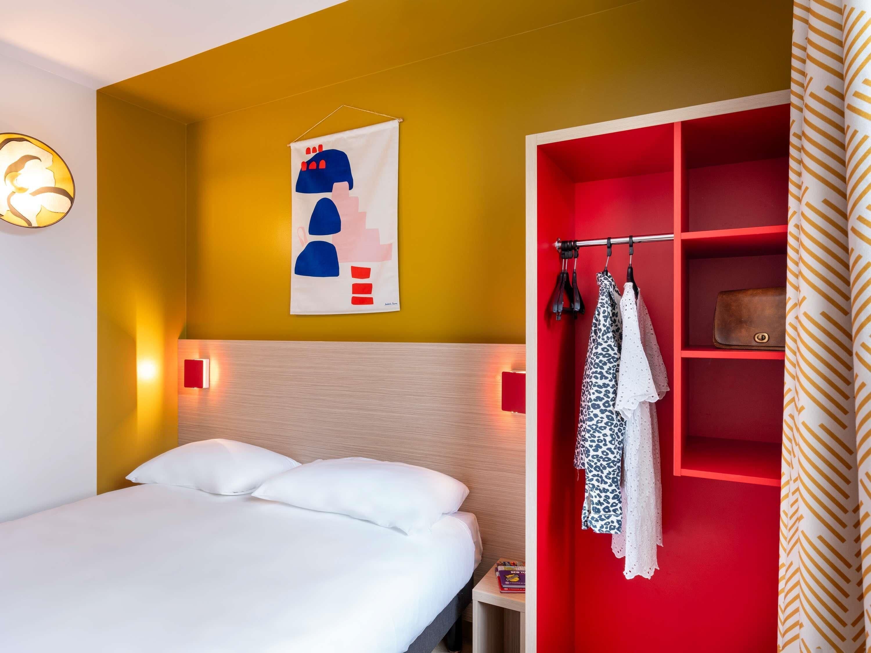 Una habitación de hotel con una cama, un armario rojo y una obra de arte colgada en la pared.
