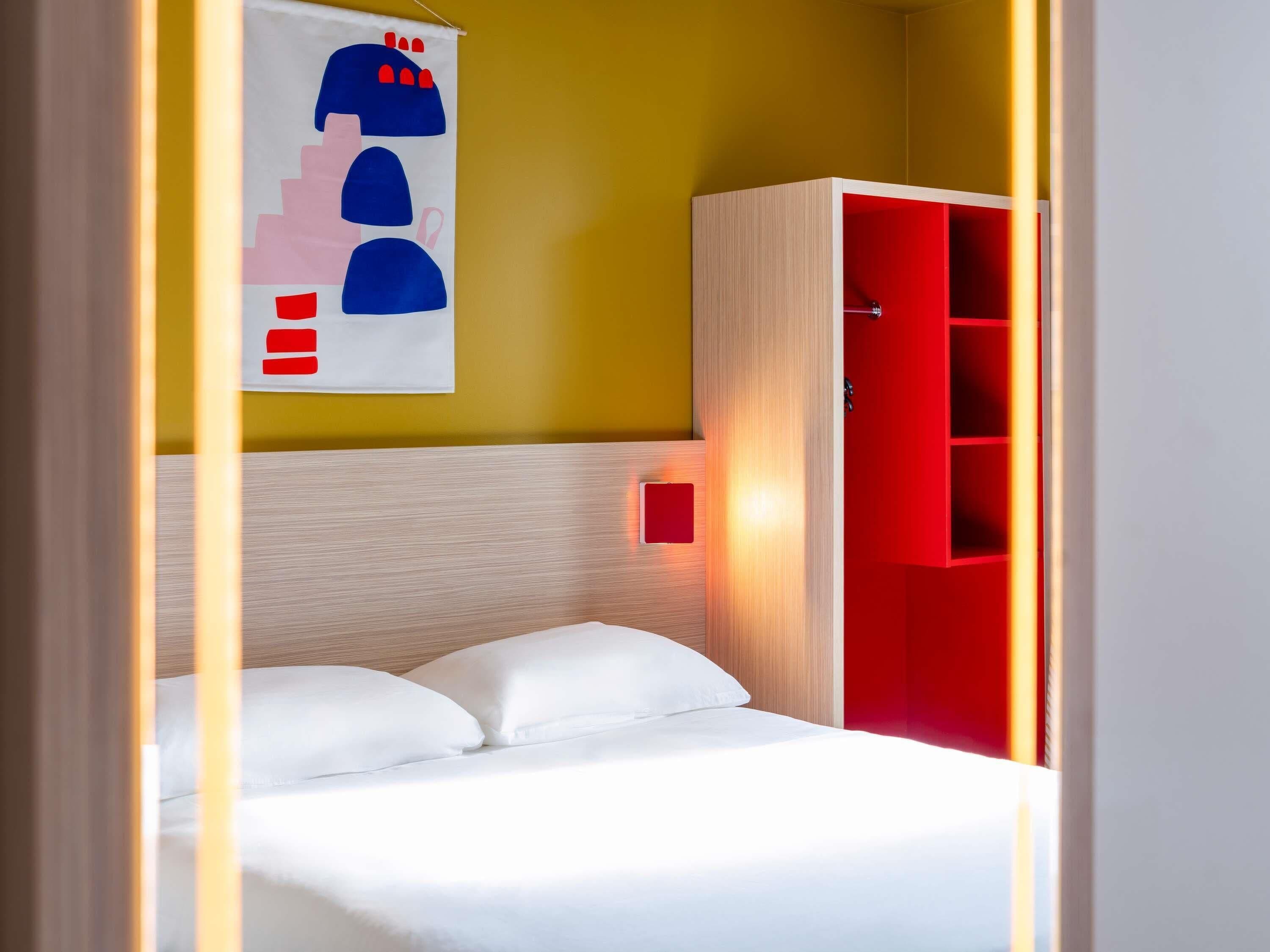 Una habitación con cama, un armario rojo y una pared con diseño geométrico.