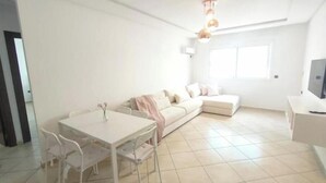 A modern living room with a white sofa, a dining table with chairs, and a TV on a stand. - Maison de Luxe Layla (Martil, Tangier-Tétouan-Al Hoceima,)