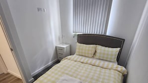 Een slaapkamer met een bed, nachtkastje en een raam met zonwering.