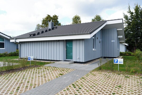 Een modern gebouw met een grijze gevel, een groene deur en een parkeerbord dat een parkeerplaats aangeeft.