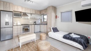 A compact kitchen with modern appliances, a bench, and a bed with a blanket. - Mayfair 246 (Cape Town)