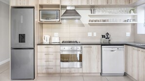 A modern kitchen with light wood cabinets, stainless steel appliances, and a black countertop. - Mayfair 246 (Cape Town)