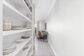A narrow hallway with white shelves holding plates and bowls, leading to a dining area with a table and chairs. - Mayfair 246 (Cape Town)