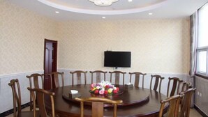 A conference room with a round table, wooden chairs, a floral centerpiece, a chandelier, and a flat-screen TV on the wall. - Huaiyuan Huiliang Mingde Hotel (Huaiyuan)