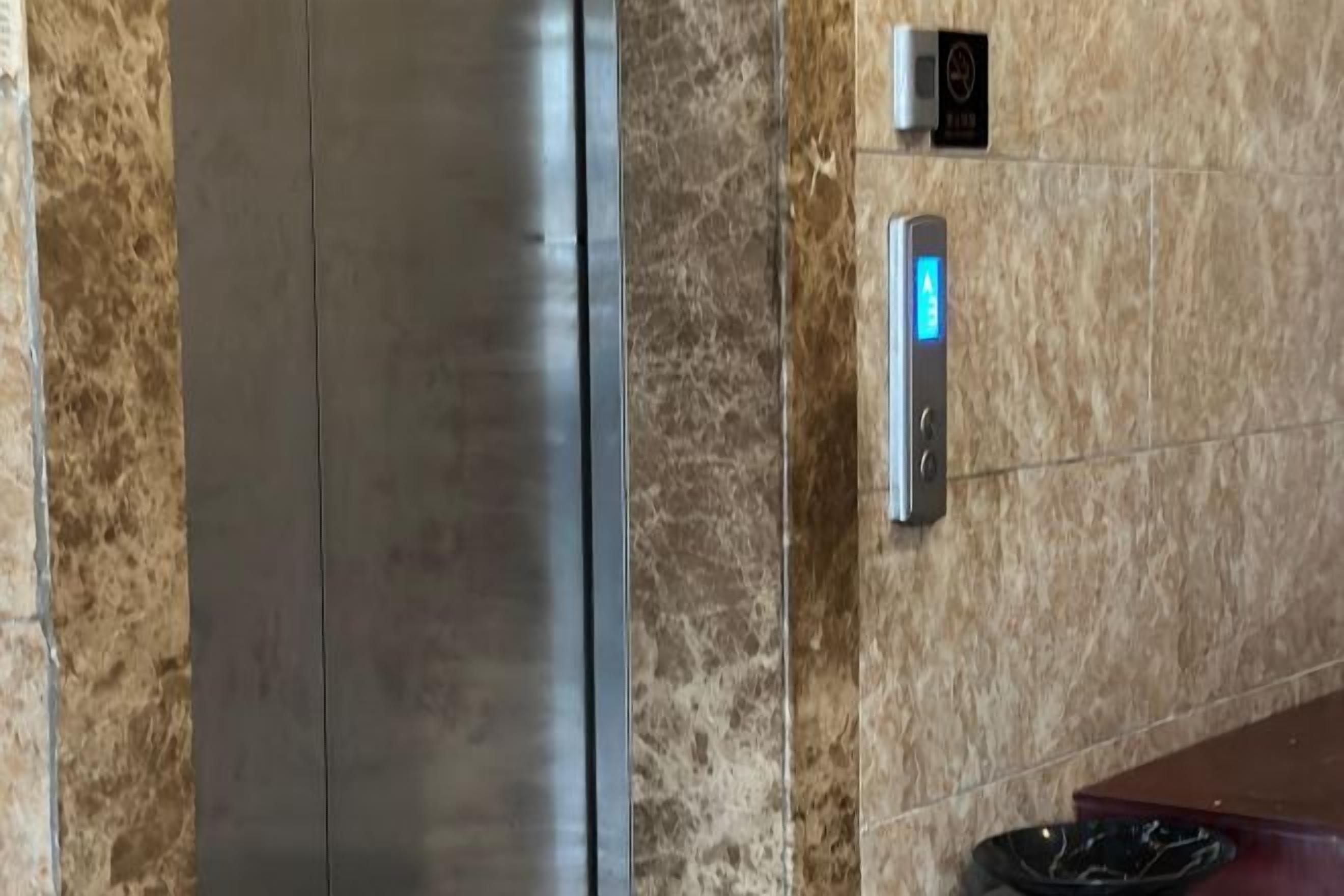 A marble wall with a metallic elevator and a digital display.