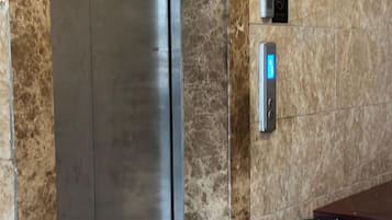 A marble wall with a metallic elevator and a digital display.