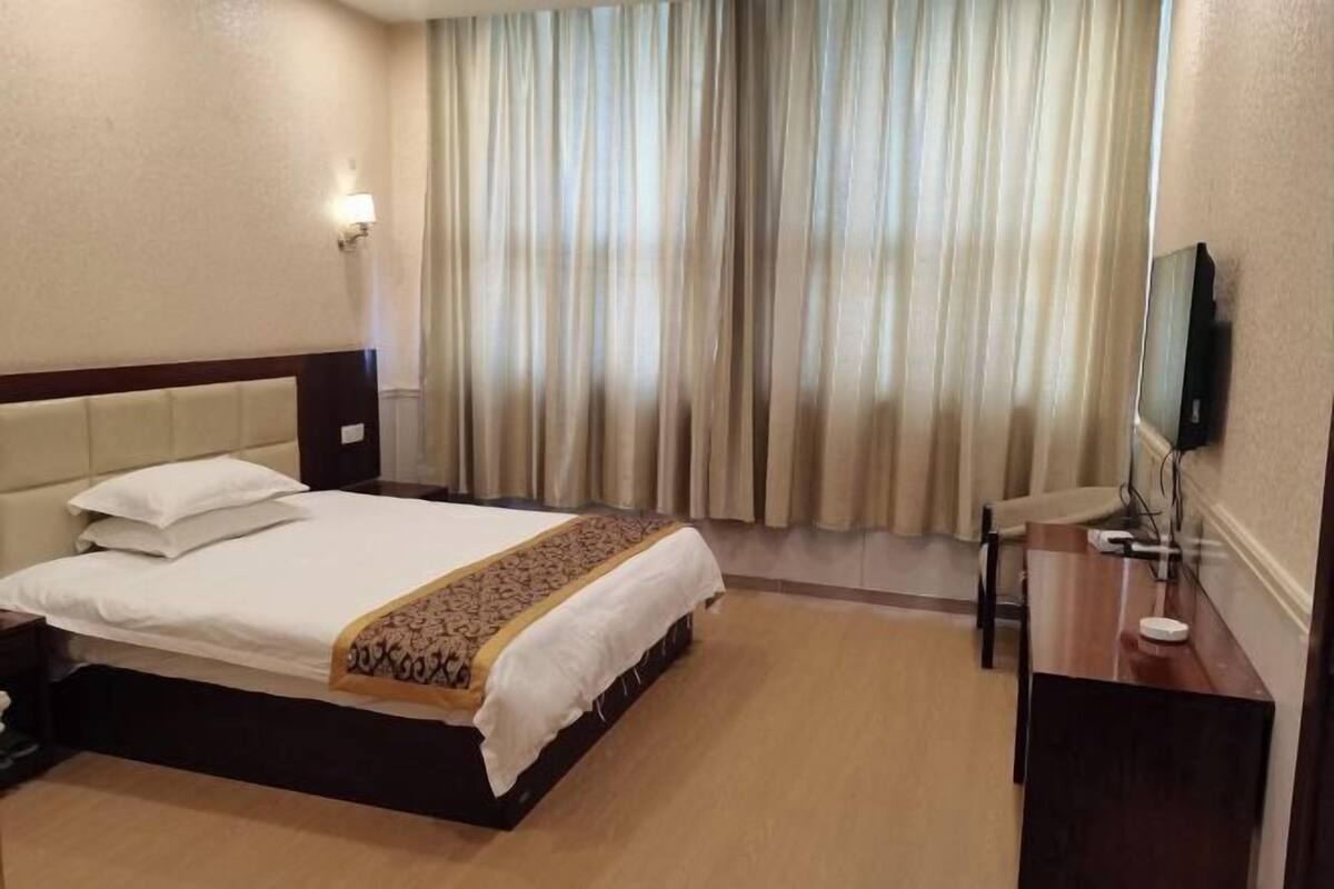 A hotel room with a bed, a desk, a television, and a window with curtains.