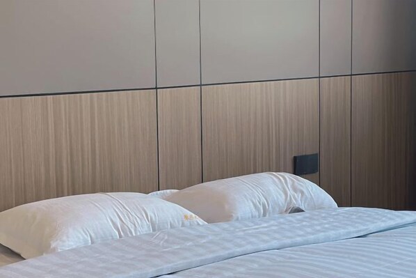 A neatly made bed with white linens and pillows, a wooden headboard, and a wall-mounted light fixture. - Huaiyuan Huiliang Mingde Hotel (Huaiyuan)