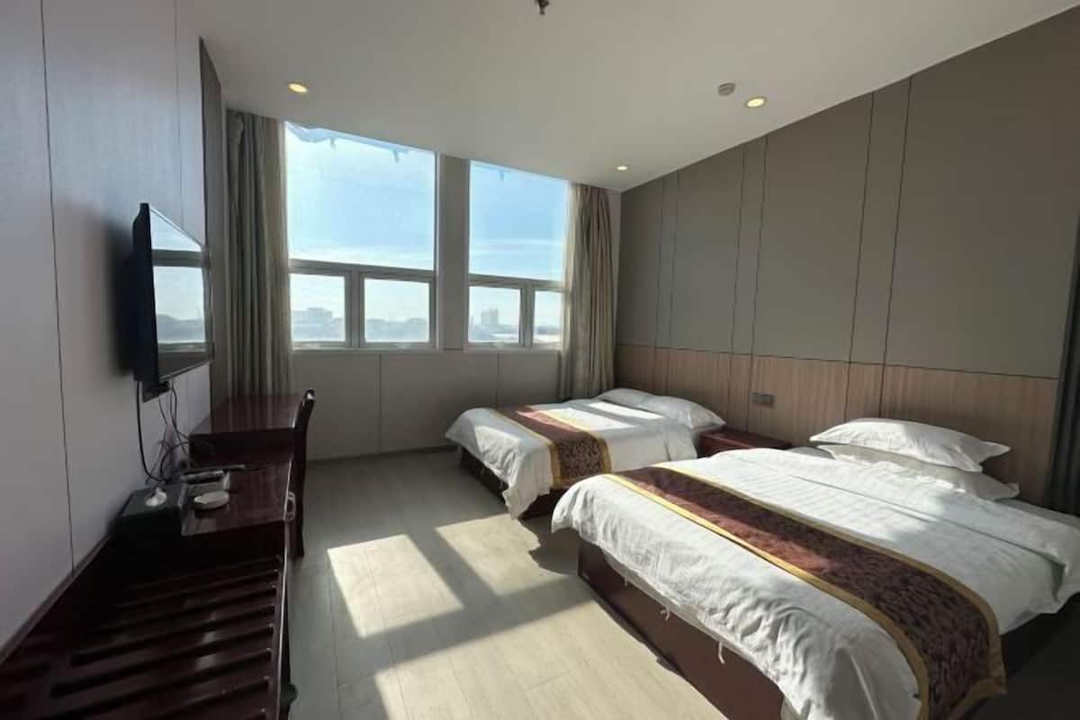 A hotel room with two beds, a desk, a TV, and large windows.