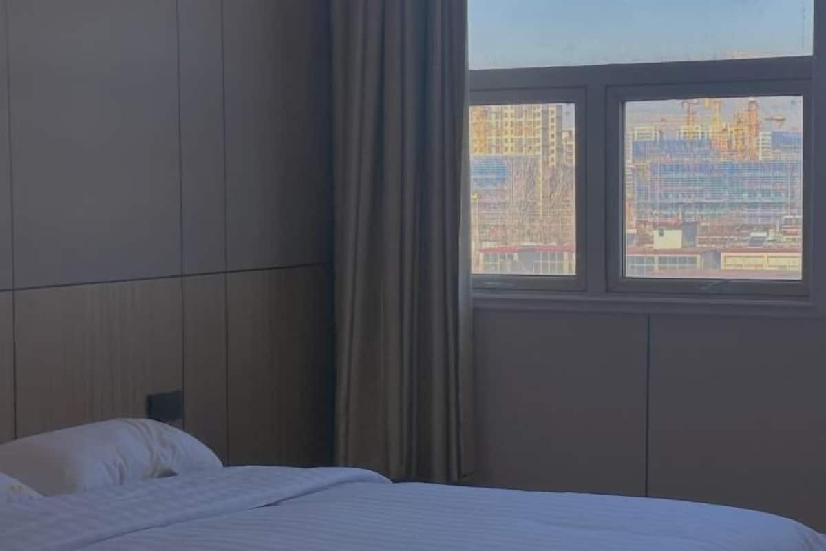 A hotel room with a bed, a window with a view of buildings, and a curtain.