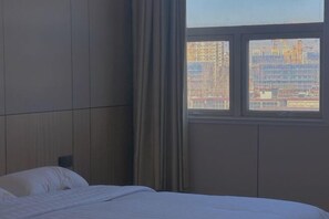A hotel room with a bed, a window with a view of buildings, and a curtain. - Huaiyuan Huiliang Mingde Hotel (Huaiyuan)